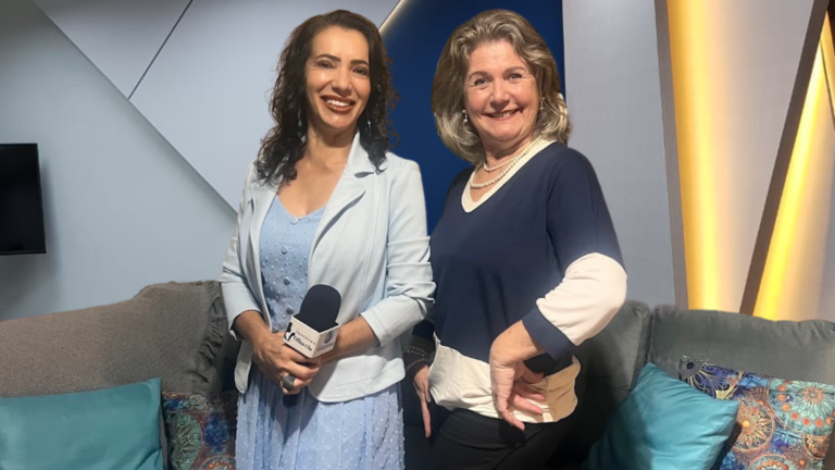 A entrevistadora Márcia Pinotti e a psicanalista Cláudia Regina Kluck sentadas em um sofá cinza no estúdio de gravação, sorrindo para a câmera. Márcia segura o microfone do programa.