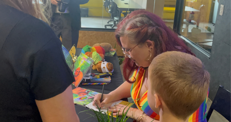 Juliana Bohrer autografa seu livro “A Capivara Ata: Entre a Luz e a Sombra” durante o evento de lançamento em Curitiba, ao lado de uma criança.