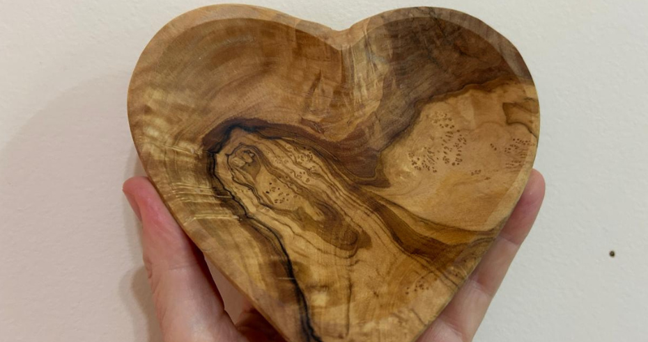 Coração de madeira de oliveira original segurado pela mão da Irmã Ketty Folli, com veios naturais e marcas internas que simbolizam feridas, resistência e vida transformada pela fé